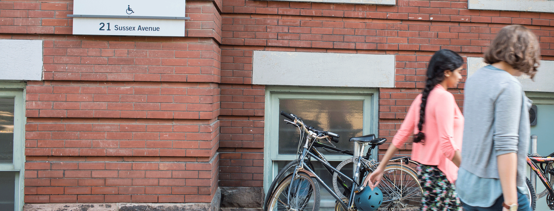 Two students walking by the red brick 21 Sussex building