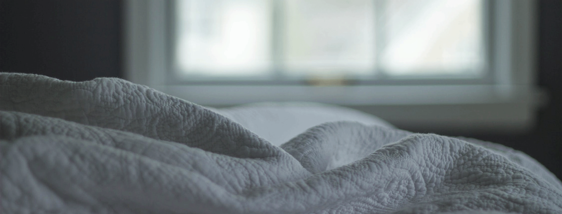 White textured bed quilt with window in background