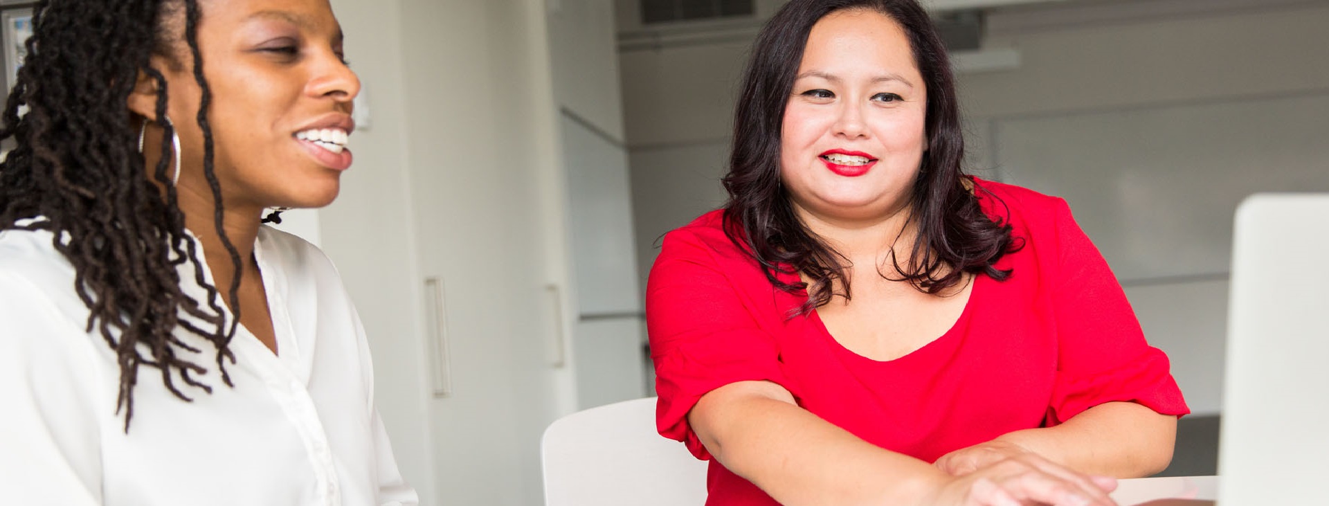 Woman wearing red top using silver MacBook with colleague